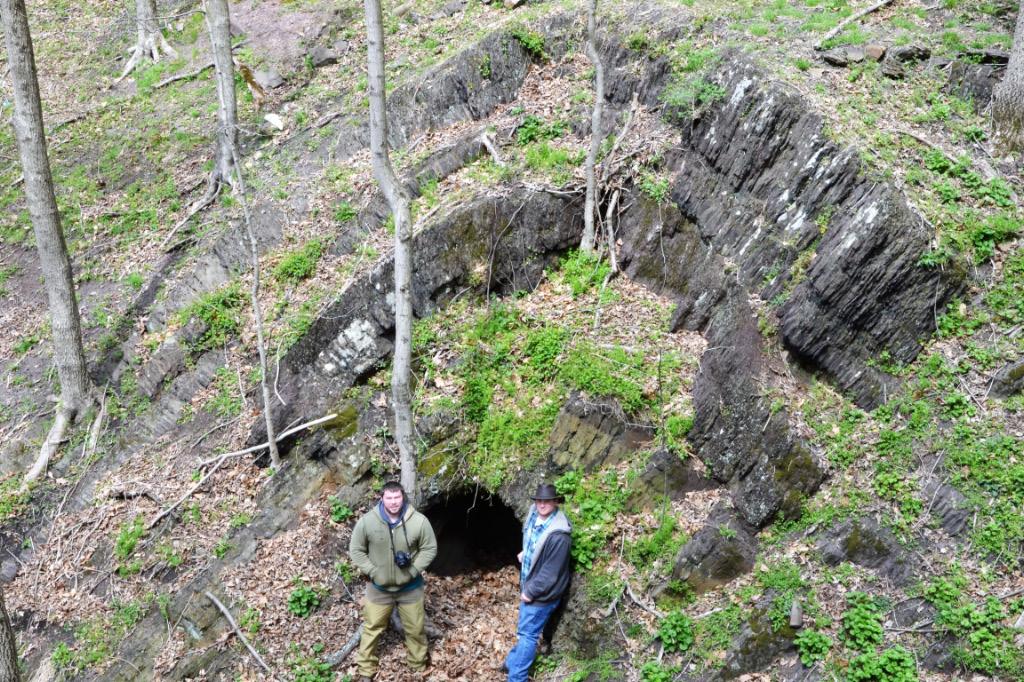 two students stand next to a cave and geological formation